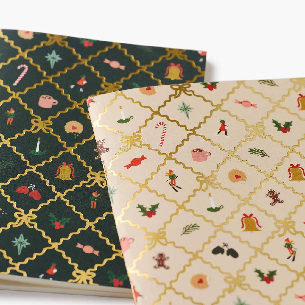 Two patterned pocket notebooks, one beige and one green, each with festive designs and gold argyle print, stacked, close-up, on a white background.