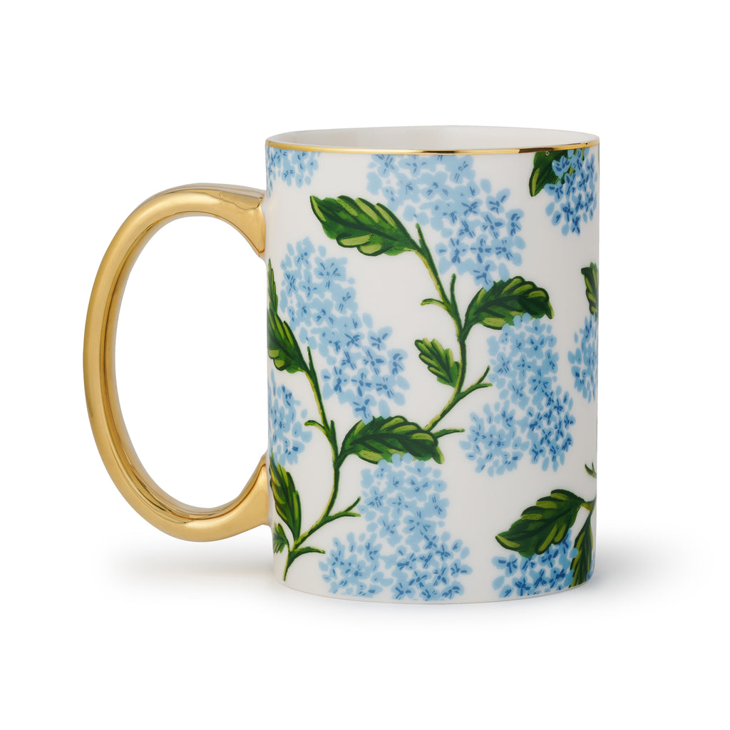 Rifle Paper Co. blue hydrangea print on white porcelain mug with gold rim and handle, handle on the left.