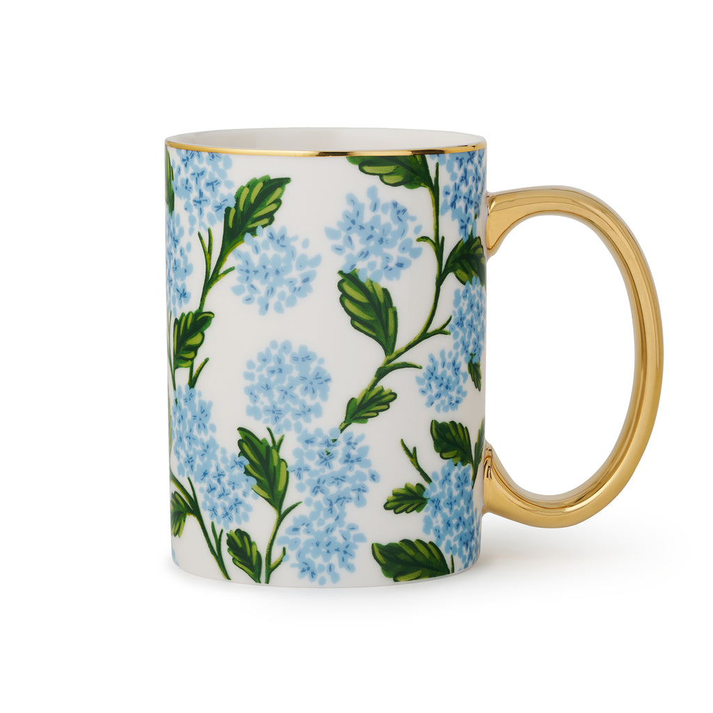 Rifle Paper Co. blue hydrangea print on white porcelain mug with gold rim and handle, handle on the right.
