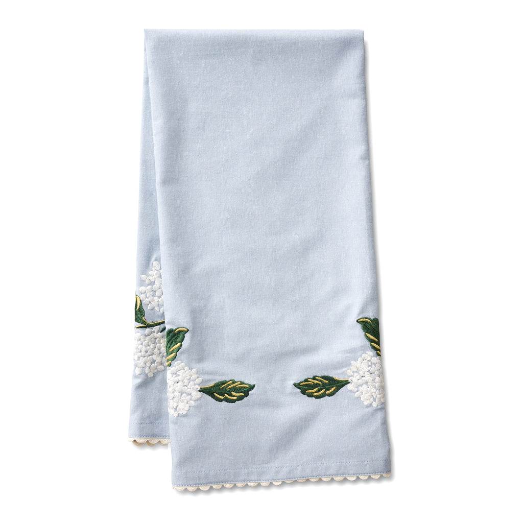 Rifle Paper Co. light blue tea towel with white hydrangea print embroidery  and white ric-rac edging, folded.