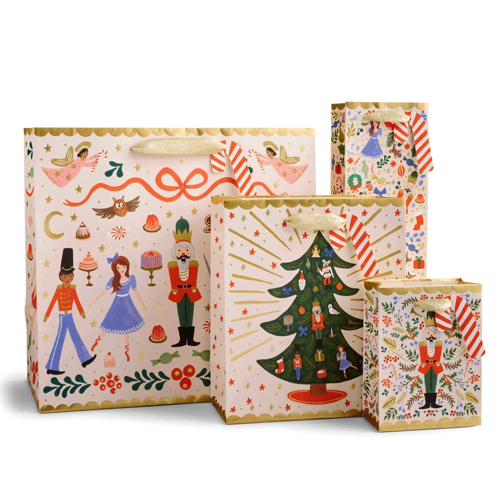 Rifle Paper Co. Nutcracker Sweets Christmas Gift Bags, in all 4 sizes. All are pale pink with assorted Nutcracker character illustrations with candy cane "to" and  "from" tag and ivory cotton ribbon handles.