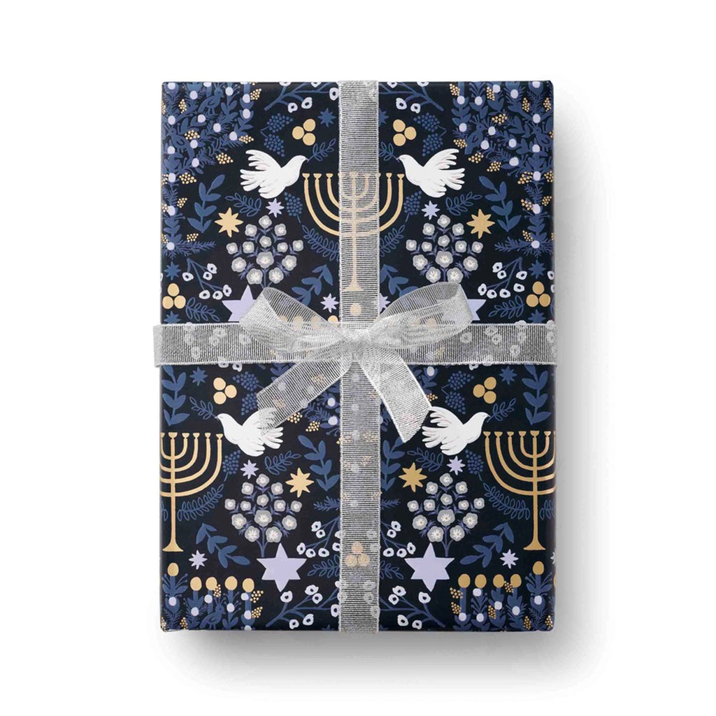 A box gift wrapped with Rifle Paper Co. Laurel Menorah Hanukkah wrapping paper and finished with a white wired ribbon bow.