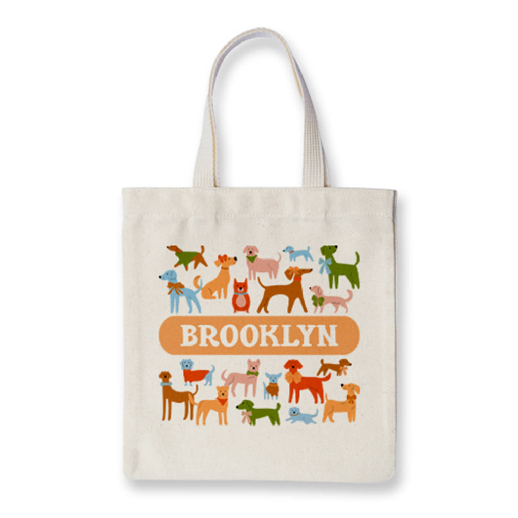 Colorful dogs in assorted shapes and sizes with "Brooklyn" in an orange bar on a natural fabric tote, on white background.