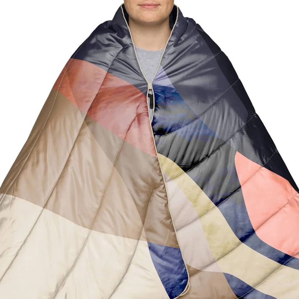 Person wrapped in a colorful puffy blanket with abstract pattern on a white background.