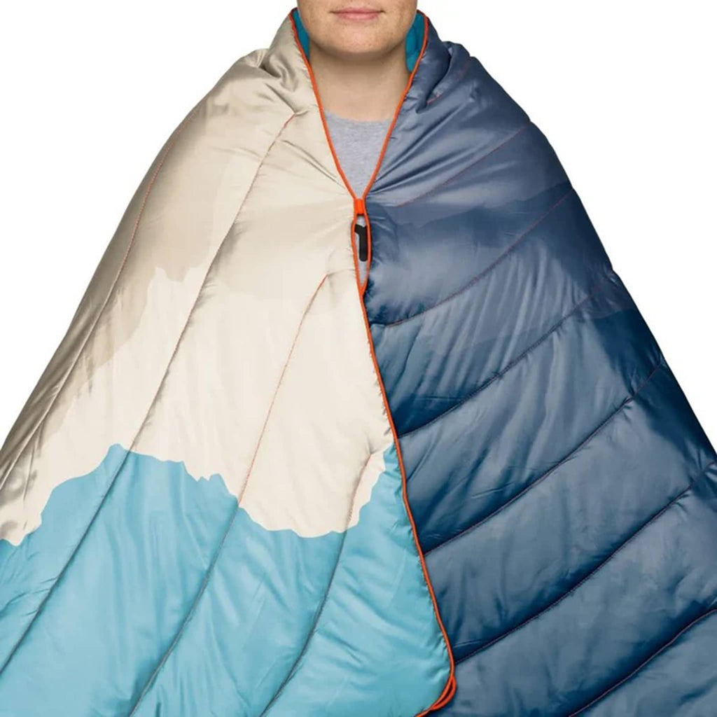 Person wrapped in a blue and beige puffy blanket, on a white background.