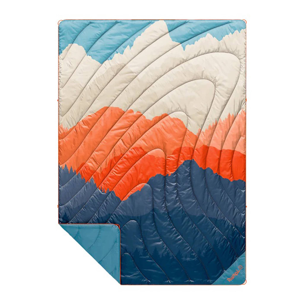 Rumpl Teton Glow original puffy blanket with an abstract mountain design in blue, orange and beige, flat with corner folded back, on a white background.