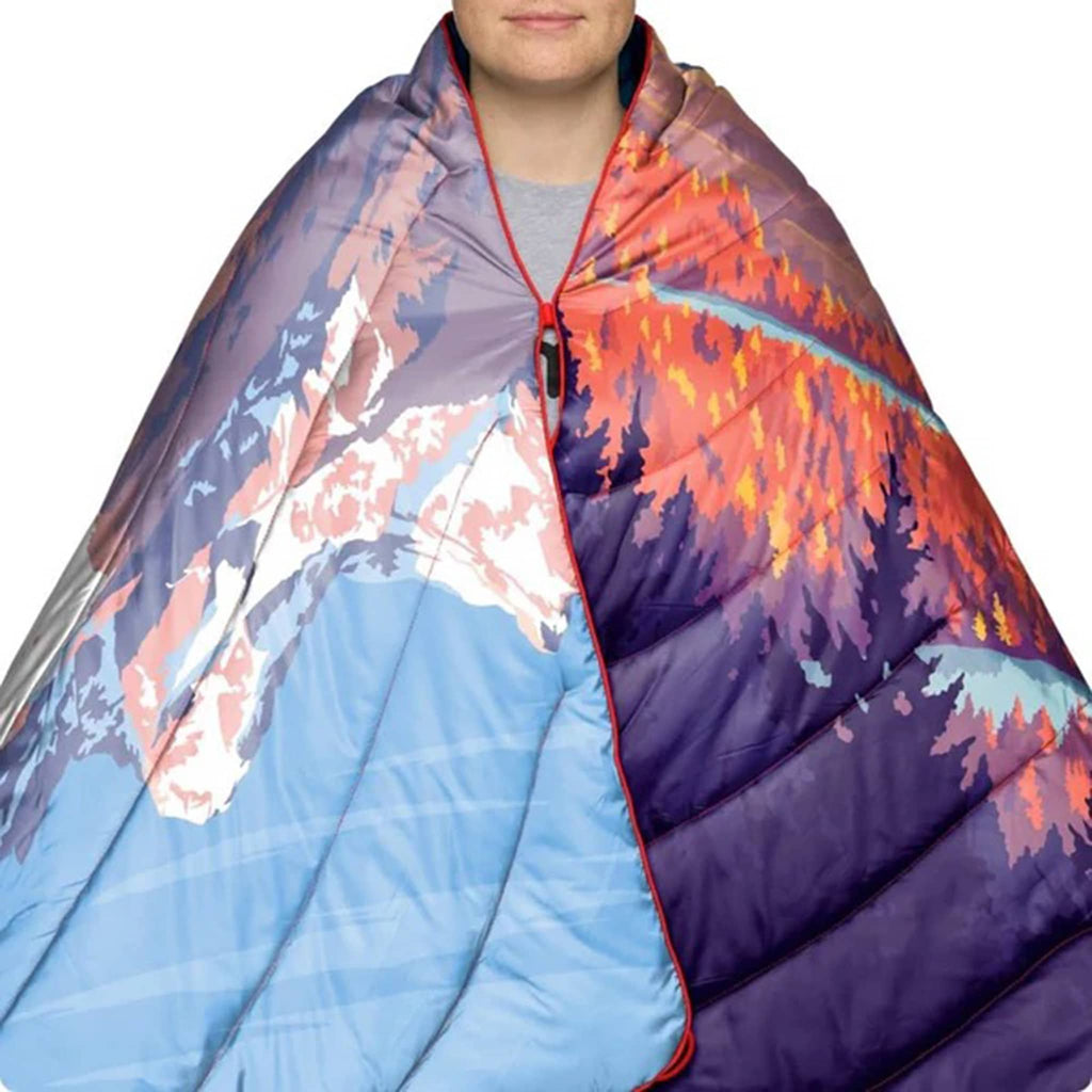 Person wrapped in a colorful quilted blanket with mountain and forest design.