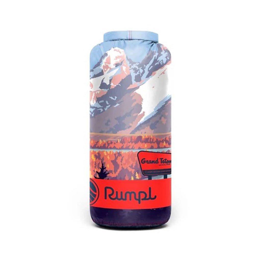 Rumpl Grand Teton National Park original puffy blanket with a mountain and lake landscape design, rolled up in stuff sack carrier, on a white background.