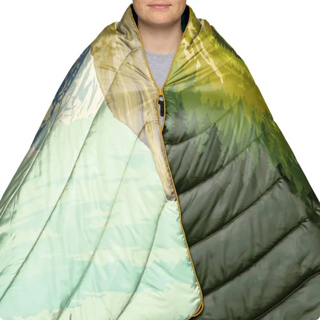 Person wrapped in a colorful puffy blanket with a gradient of green, blue, and beige.