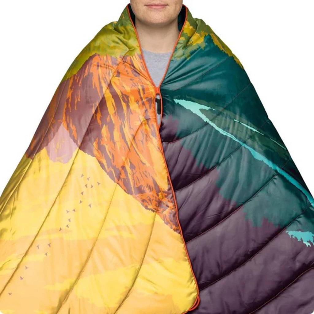 Person wrapped in a colorful puffy blanket with a gradient of orange, green, and purple on a white background.