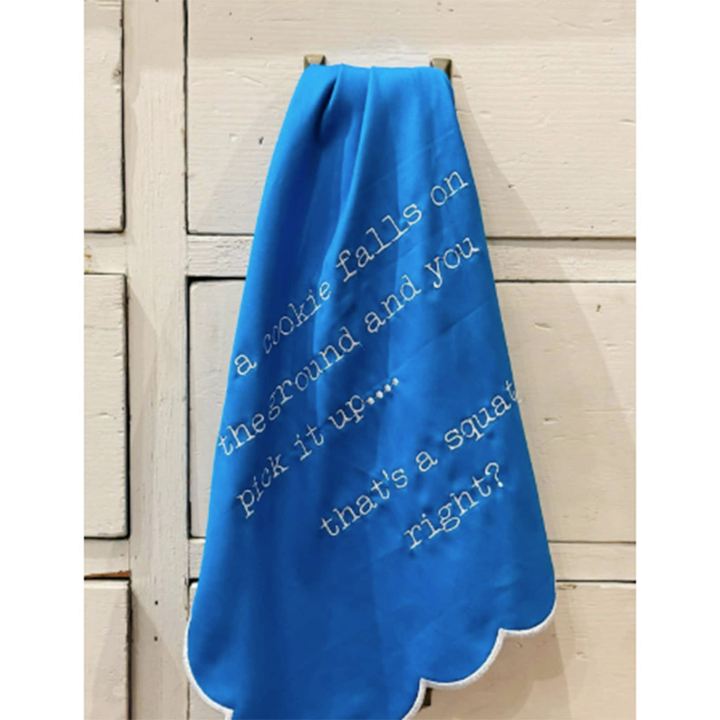 Blue towel with humorous text hanging on a handle on wooden drawers.