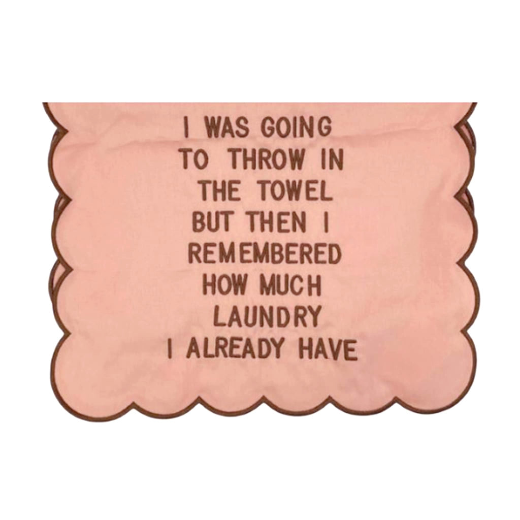 Dusty pink scallop edge tea towel with brown text 'I WAS GOING TO THROW IN THE TOWEL BUT THEN I REMEMBERED HOW MUCH LAUNDRY I HAVE' and brown trim, on a white background.