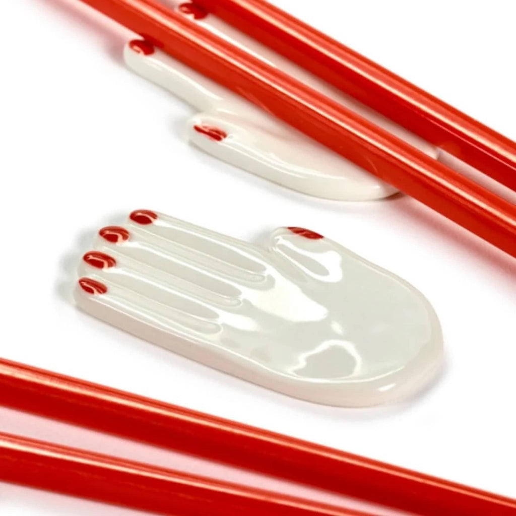White porcelain hand-shaped chopstick holder, close-up with and without red chopsticks.