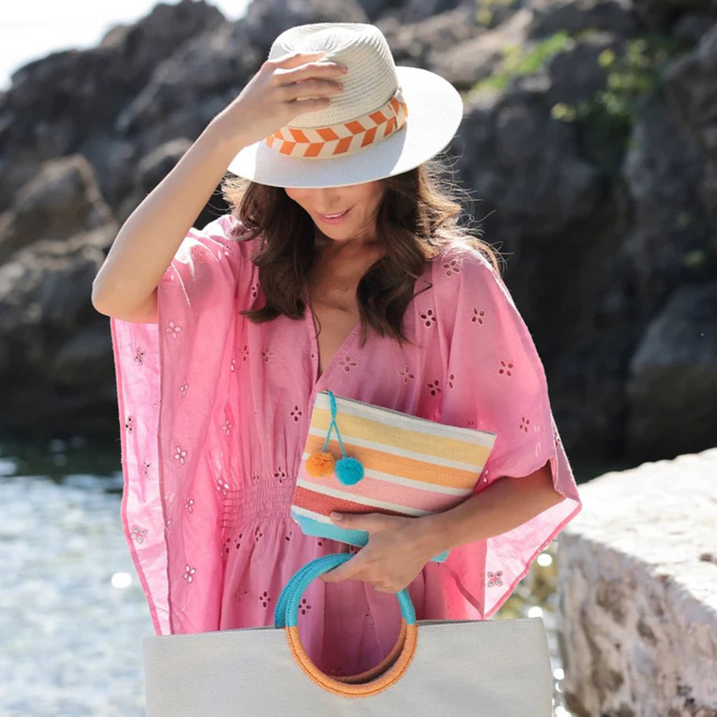Shiraleah Aramis hat in crisp ivory woven straw with cream and orange band, on model's head on the beach.