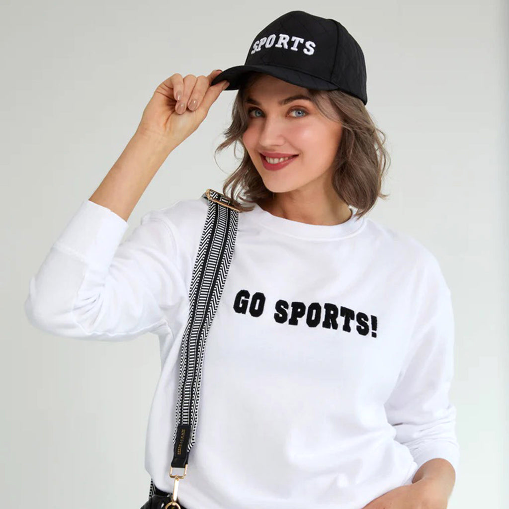 Shiraleah black quilted ball cap with "sports" in white lettering on the front, on a model.