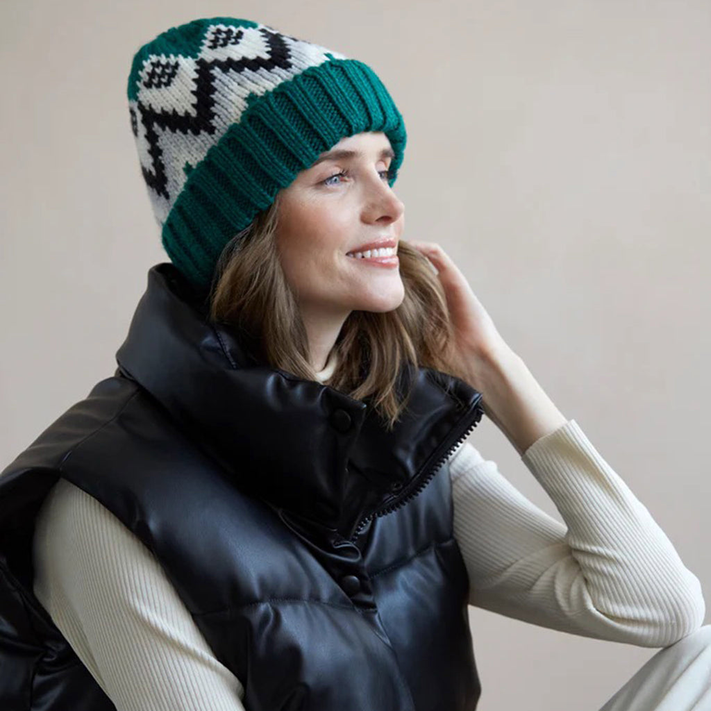Shiraleah Andy Knit Winter Hat in green with white, gray and black design on model wearing a white ribbed shirt and black puffy vest.