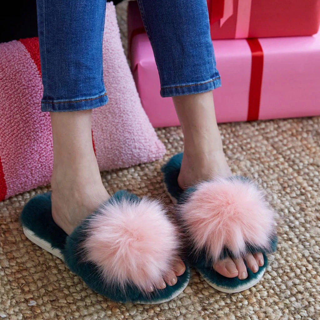 Shiraleah Amor Holiday Slippers, dark green plush slides with fuzzy pale pink pompom on top band, shown on feet.