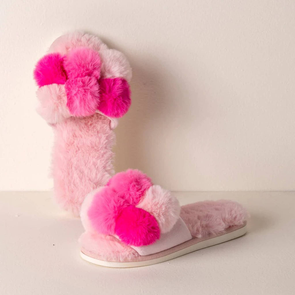 Shiraleah Carina fluffy pink slipper slides with pompoms in shades of pink, on a pink background.