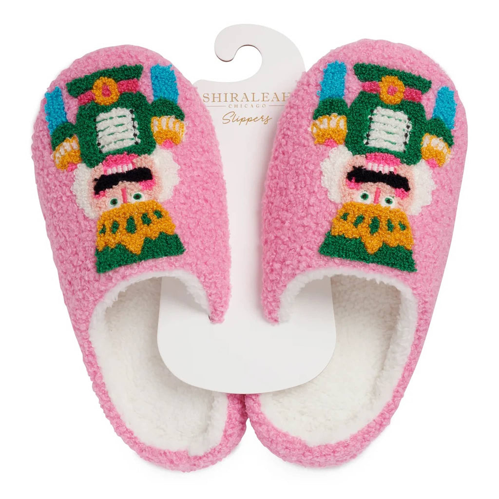 Pair of pink slippers with a nutcracker design, on hanger, on a white background.