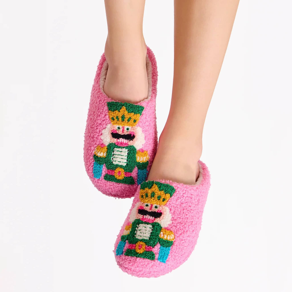 Pink slippers with nutcracker design on a persons feet, on a white background.