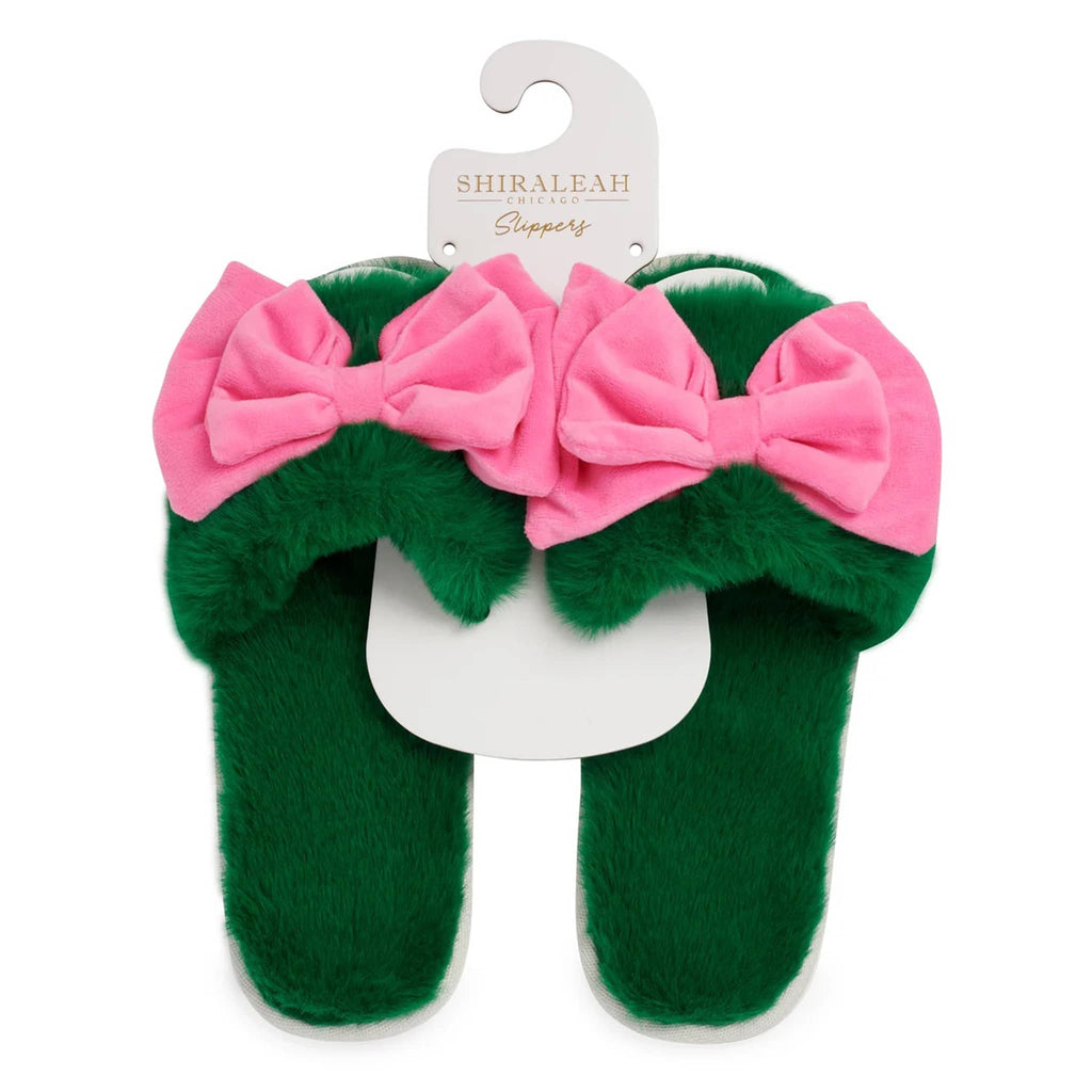 Green fuzzy slippers with pink bows on a white background, featuring the brand 'Shiraleah'.
