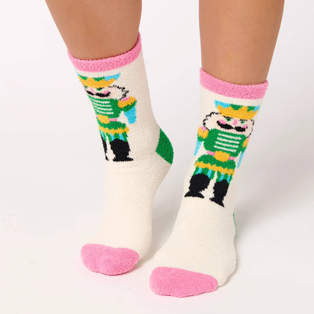 Pair of ivory socks with colorful nutcracker design and pink cuff and toe, on a person's feet, on a white background.