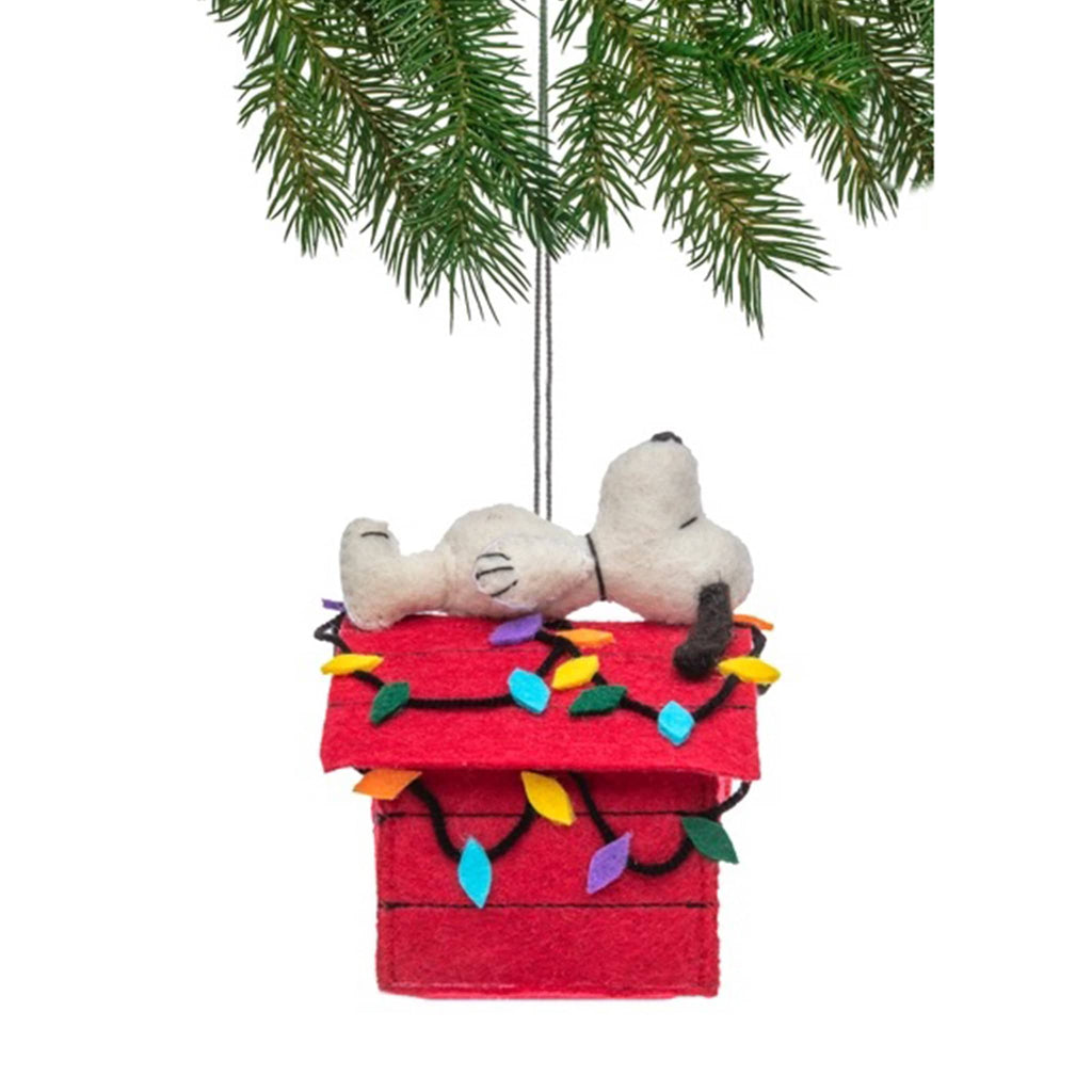 Christmas ornament with snoopy lying on the roof of his red doghouse with colorful lights, hanging from a tree branch.