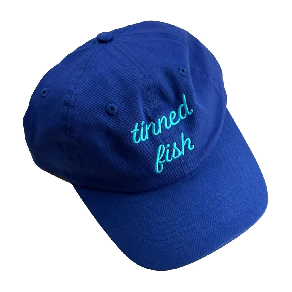 Bright blue cap with 'tinned fish' embroidered in turquoise, on a white background.