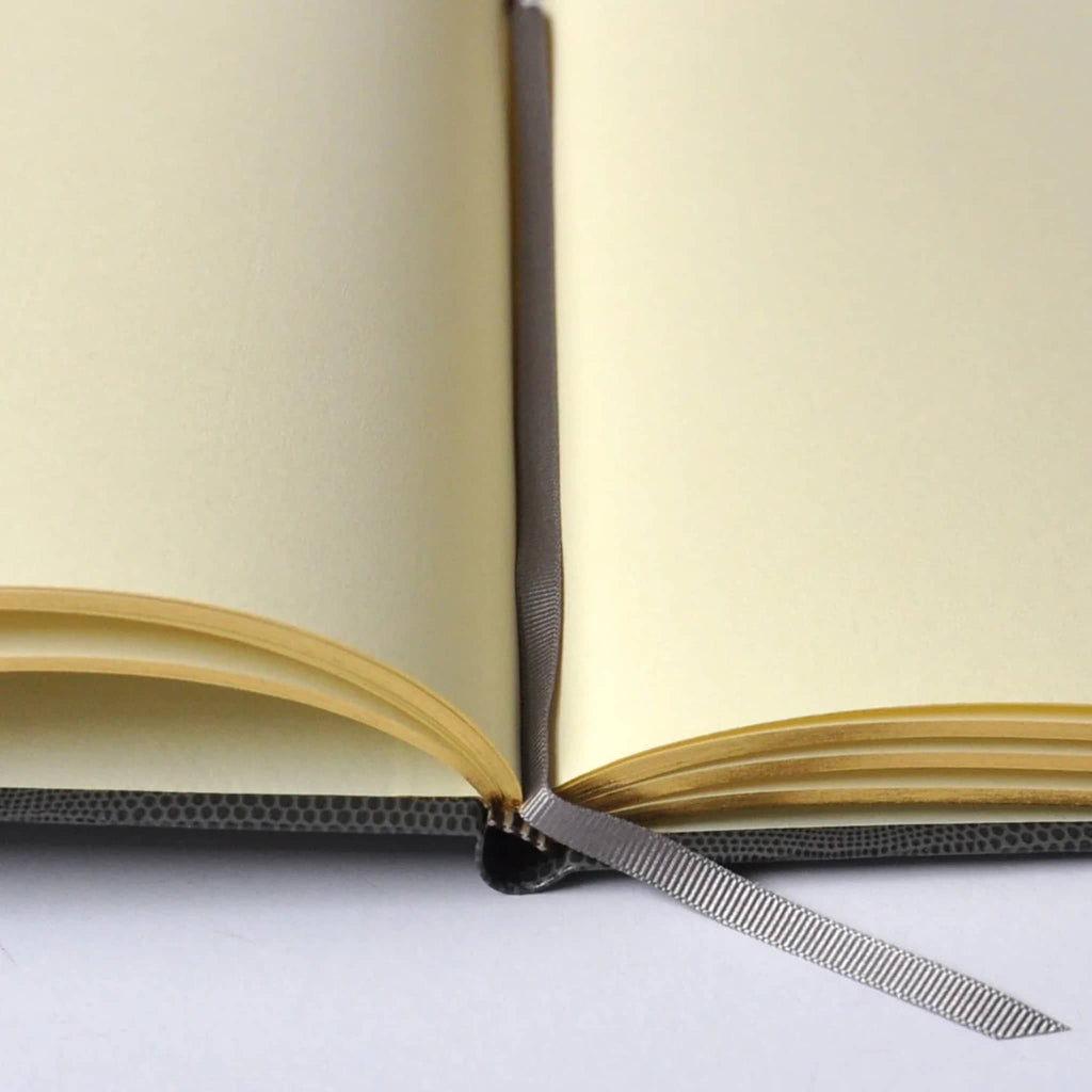 Open notebook with cream unlined pages and a gray ribbon page marker, on a white background.
