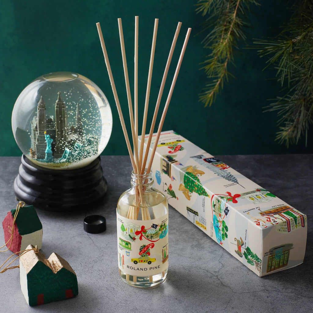 Diffuser with sticks, snow globe, and box packaging on a dark surface with green background.