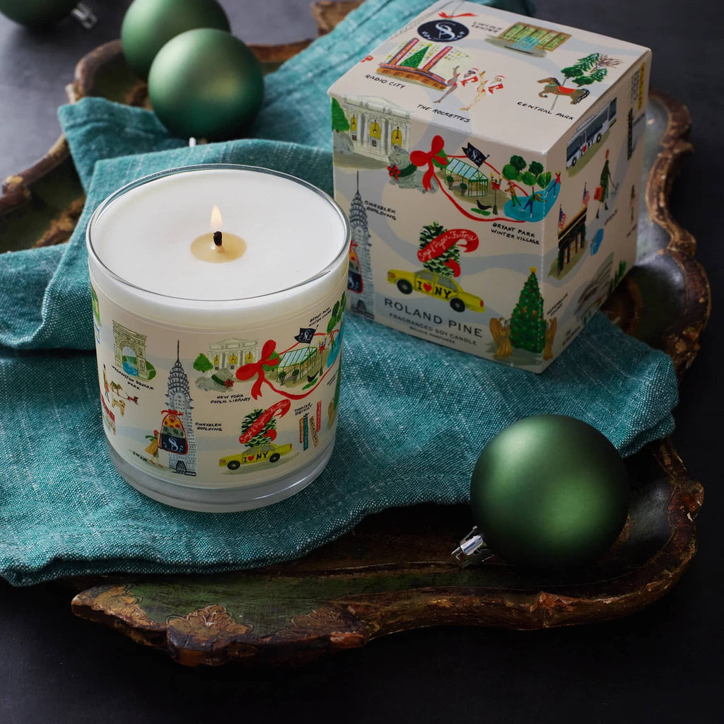 Candle with decorative packaging and green ornaments on a wooden surface.