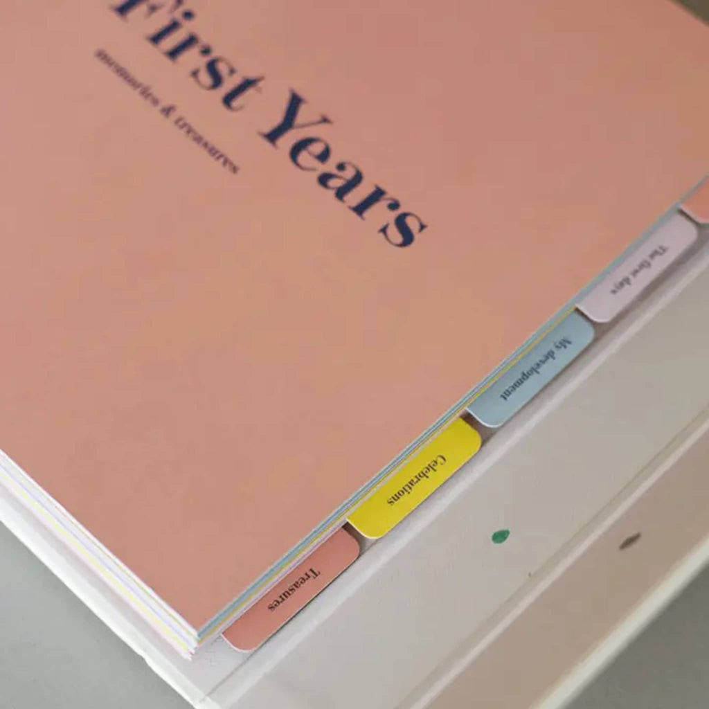 Memory book titled 'First Years' with colorful tabs on a light gray background.