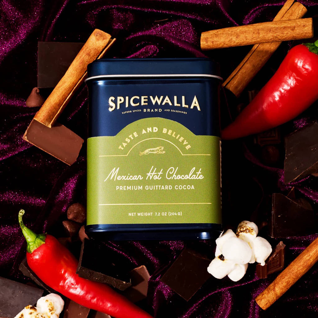 Spicewalla Mexican Hot Chocolate can surrounded by spices and peppers on a dark background.