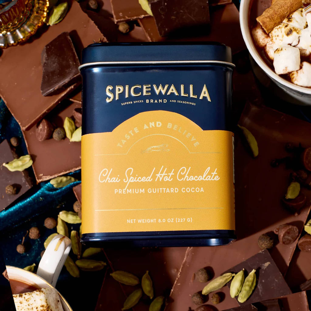 Spicewalla Chai Spiced Hot Chocolate canister surrounded by chocolate pieces and spices.