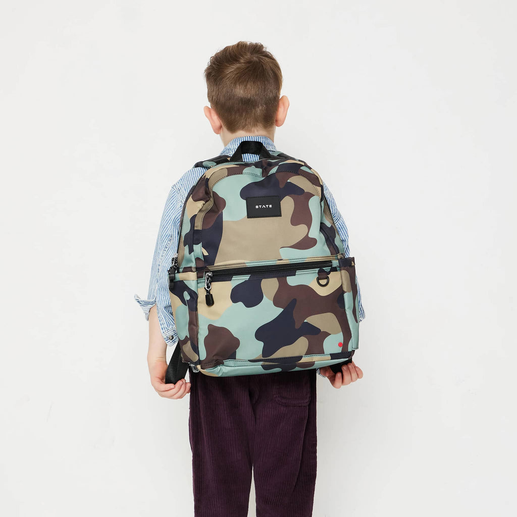 State Bags Kane Kids Double Pocket Backpack in Camo, on child's back to show size.
