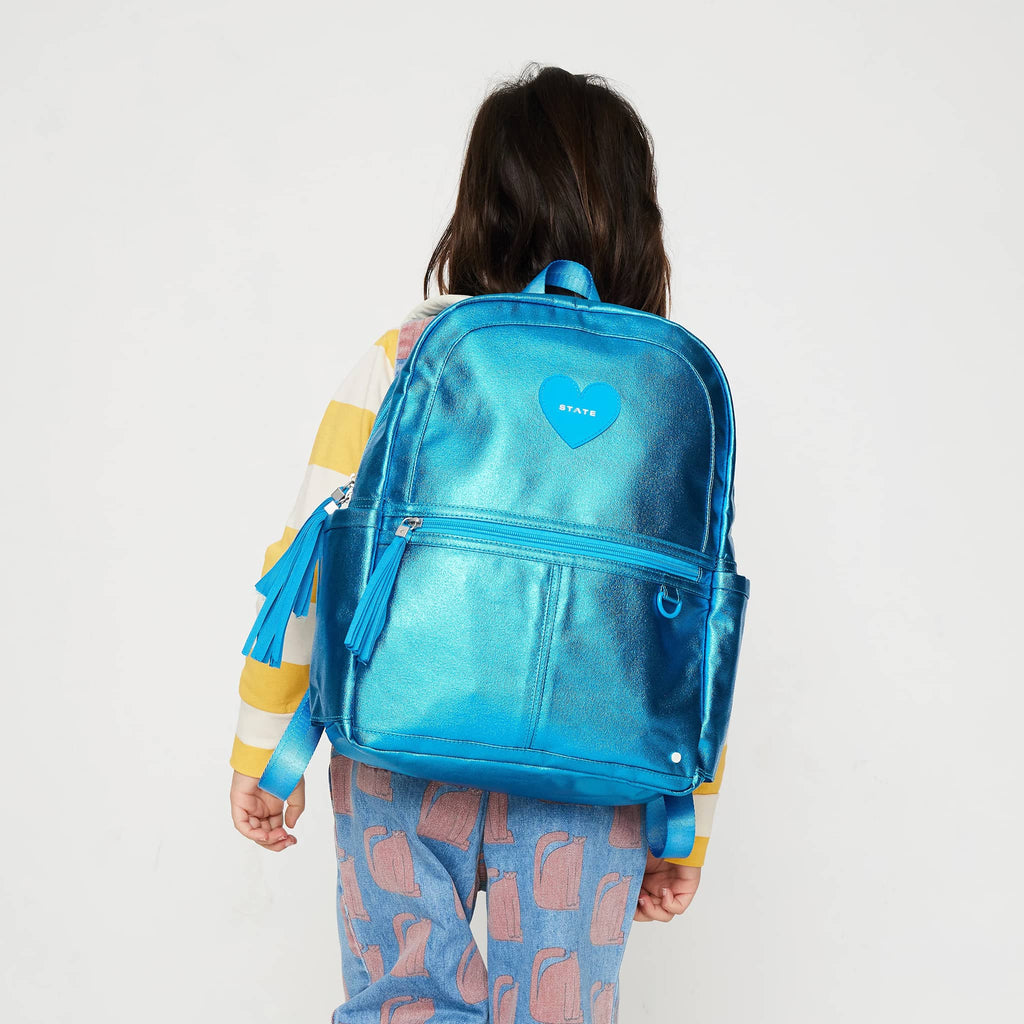 State Bags Kane Kids Travel Backpack in blue metallic, on child's back to show scale.