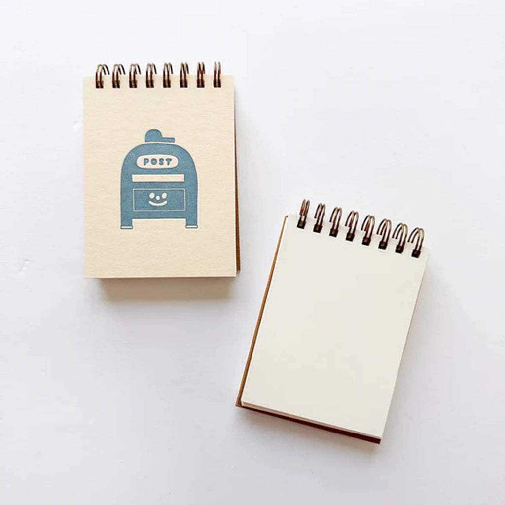 Two small spiral-bound notebooks on a white background, one with a blue postbox design.