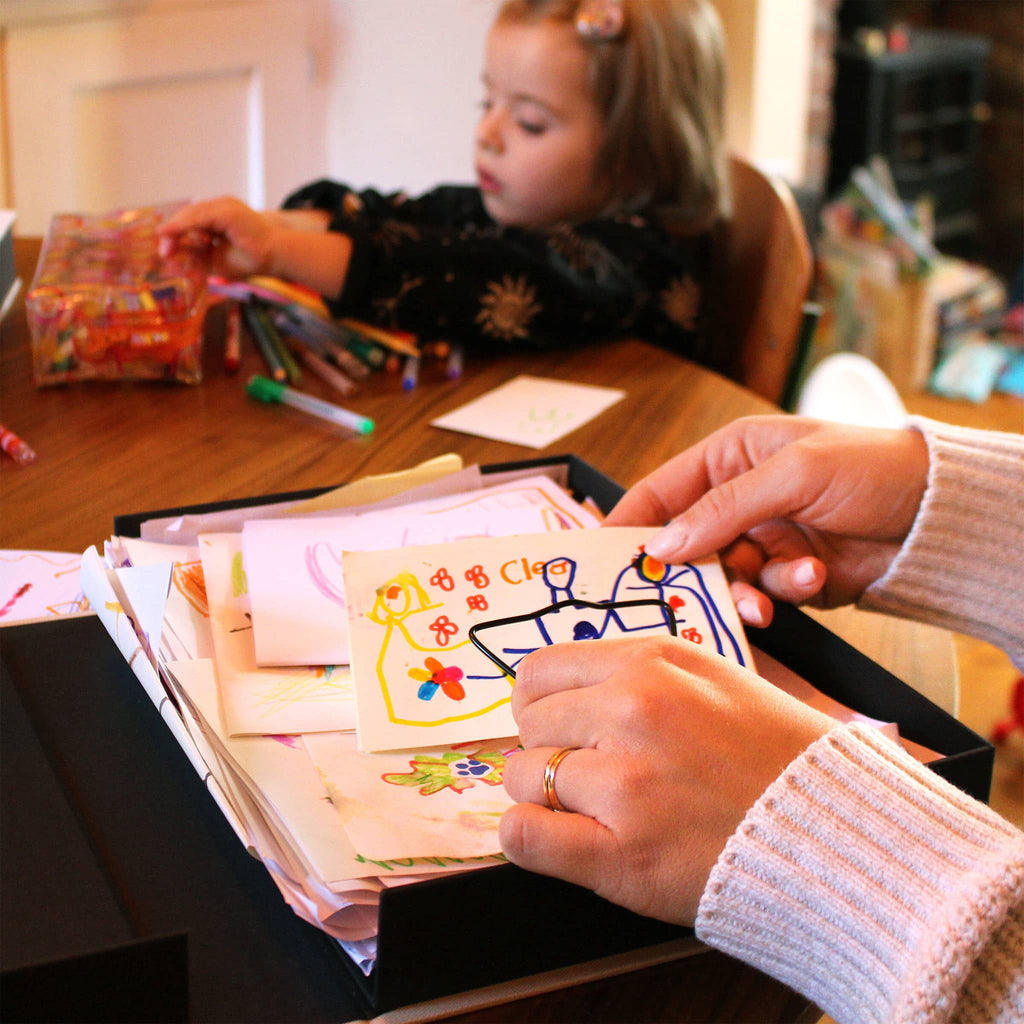 Person and child looking at children's drawings in a box.