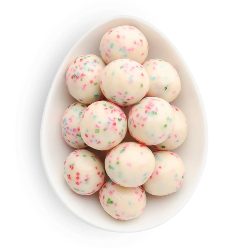 Sugarfina Holiday Presents Sprinkle Cookies candy in a white oval dish, candies look like round white chocolate balls with red, pink, blue and green sprinkles.