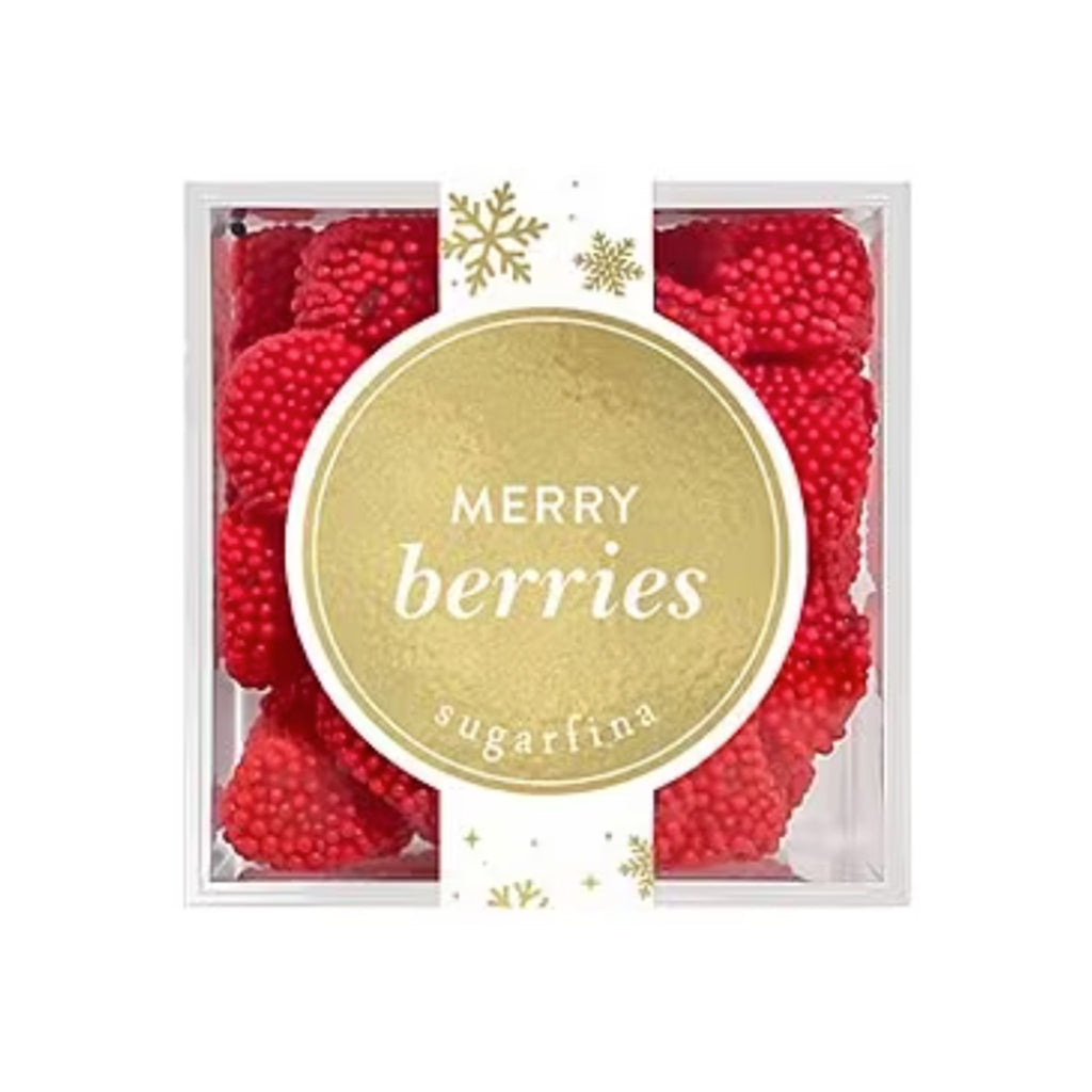 Top view of Sugarfina Merry Berries gummy candy in clear acrylic candy cube with gold circular label and a white and gold snowflake print ribbon label running down the middle.