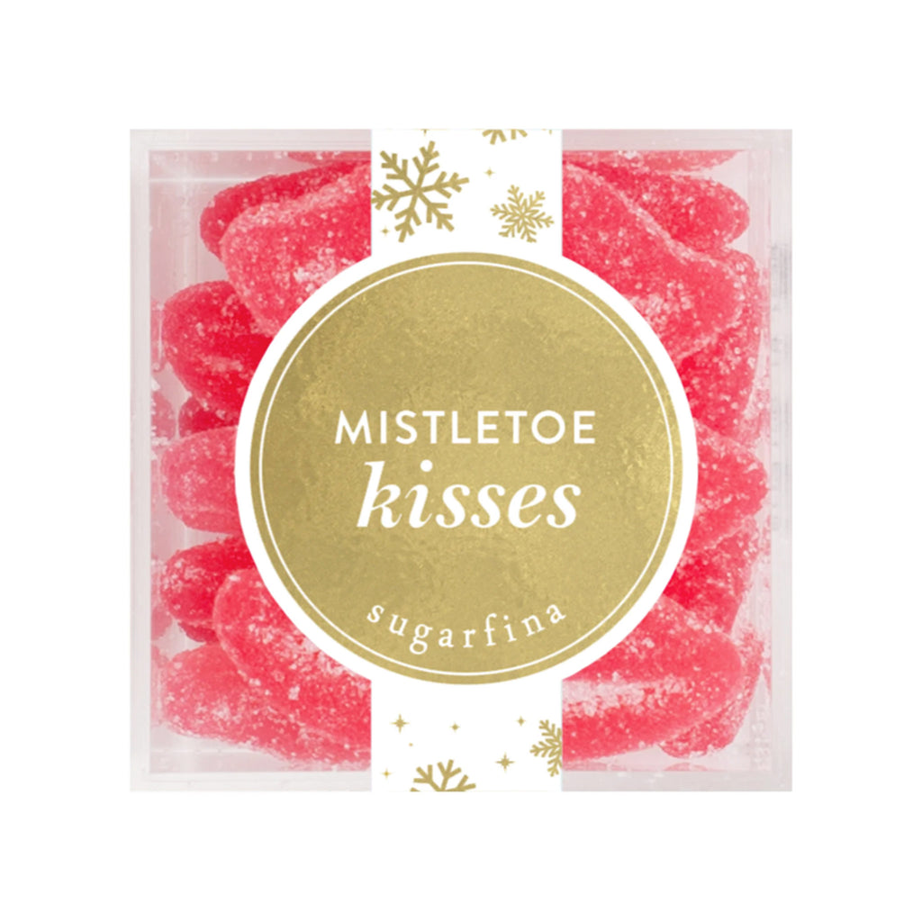 Top view of Sugarfina Mistletoe Kisses Sugar Lips holiday gummy candy in small clear acrylic candy cube with a gold circular label on the top and a gold snowflake pattern on a white ribbon sticker.