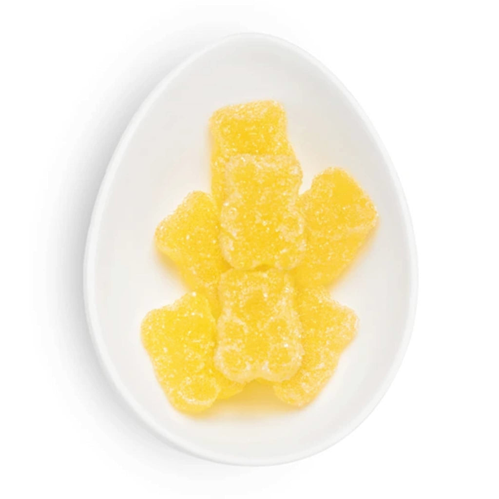 Yellow gummy bears dusted with sugar crystals, on a white oval plate on white.