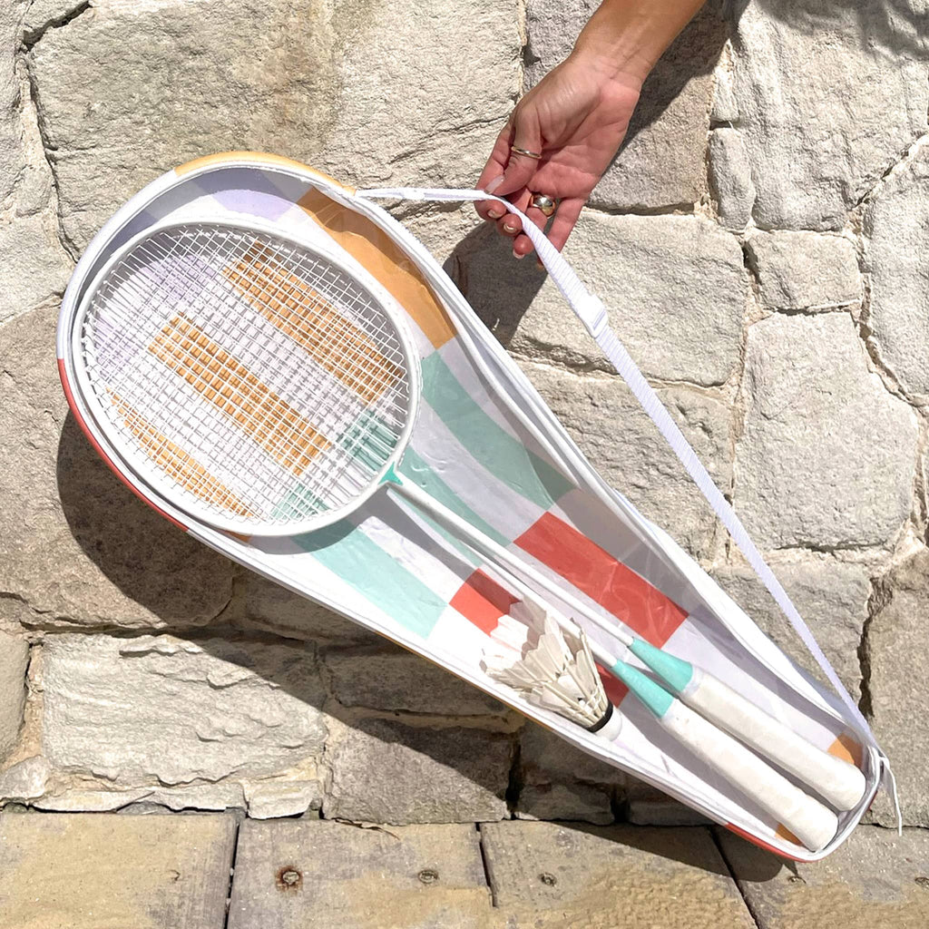 Sunnylife Rio Sun Multi Badminton set with 2 white racquets, 2 shuttlecocks in a bright striped carry bag, outside with model holding by the strap.