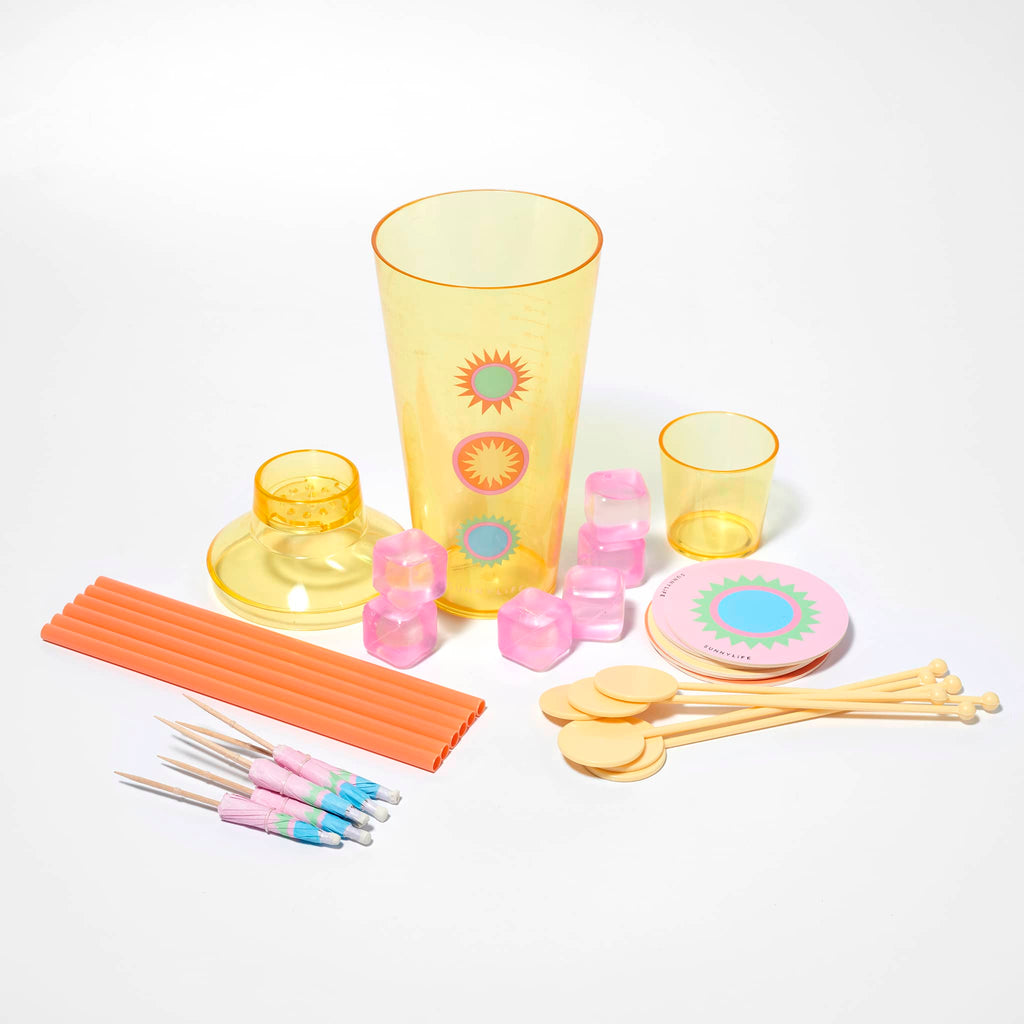 Sunnylife Rio Sun Cocktail Essentials kit,  yellow acrylic cocktail shaker with cap and strainer, pink chill cubes, stirrers, umbrellas, straws and coasters.