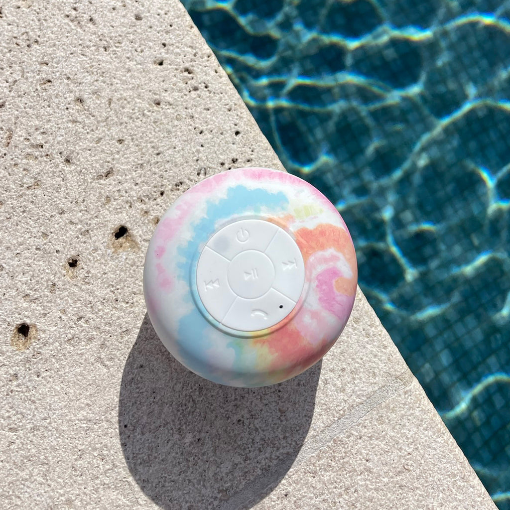 Sunnylife Rainbow Tie Dye Waterproof Splash Speaker, front view, shown poolside.