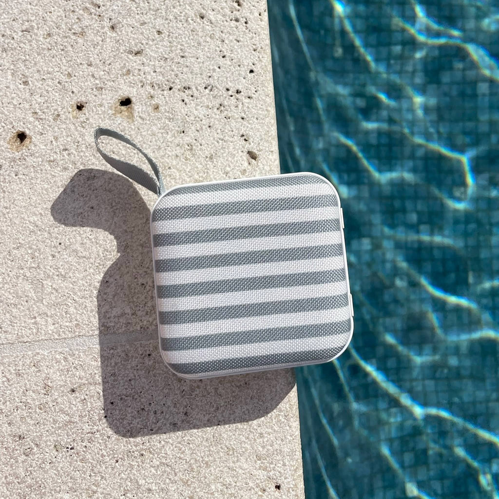 Sunnylife Portable Travel Speaker in The Vacay Olive and Cream Stripe, front view laying poolside.