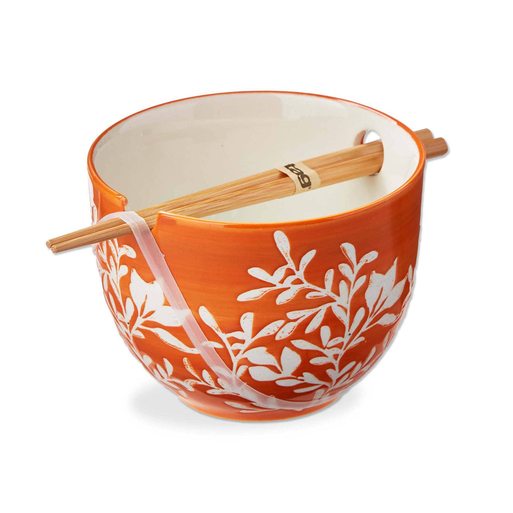 Orange ceramic bowl with white leaf pattern and wooden chopsticks on a white background.