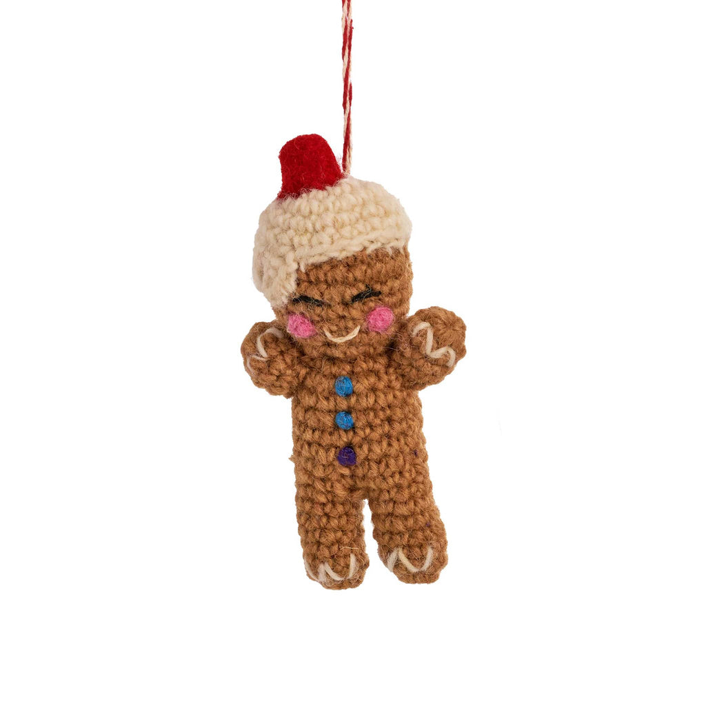 Crocheted gingerbread man ornament with a white and red pompom on a white background.