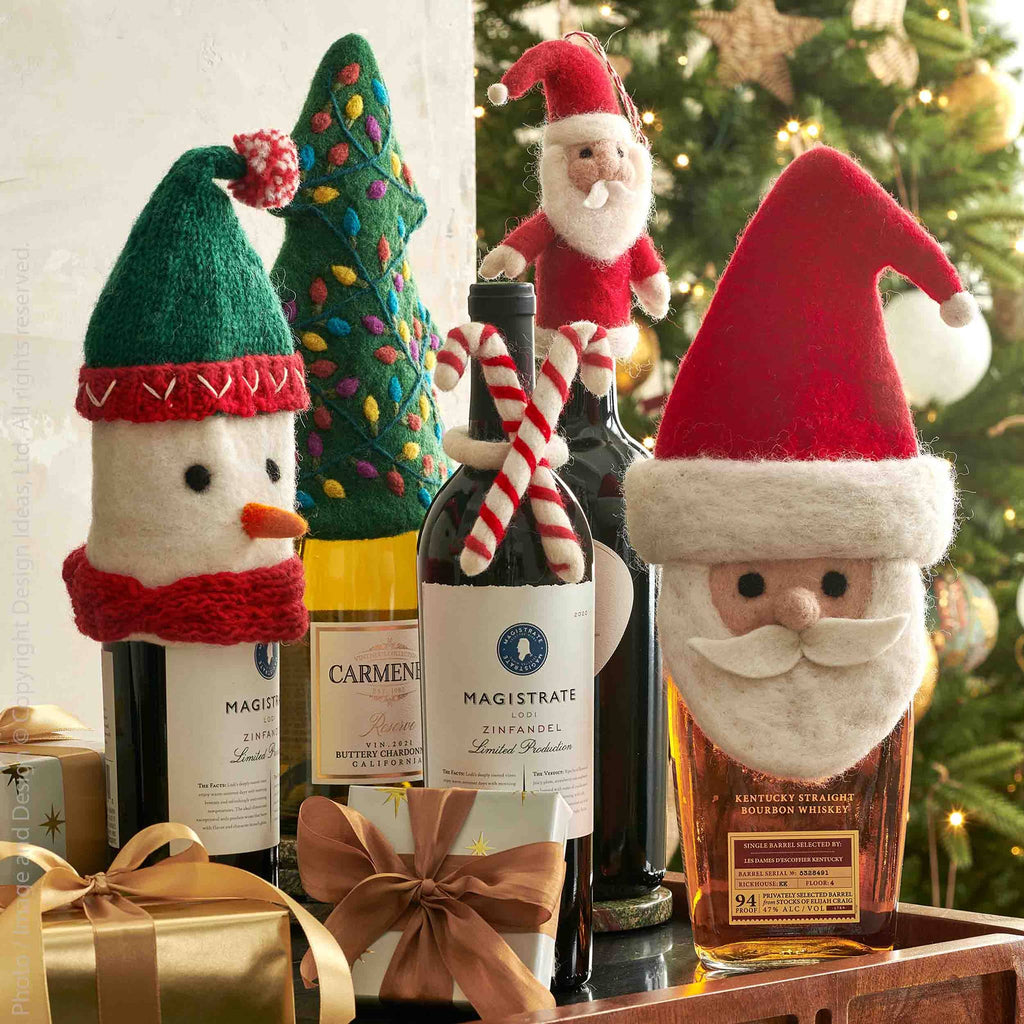 Wine bottles with festive bottle covers and decorations in front of a Christmas tree.