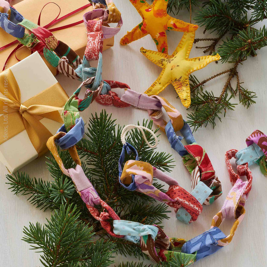 Colorful fabric garland on a Christmas tree with wrapped gifts in the background.